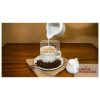 A cup of black coffee with cream on a table with beans